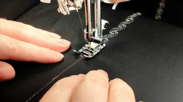 Hände führen Stoff in der Nähmaschine.